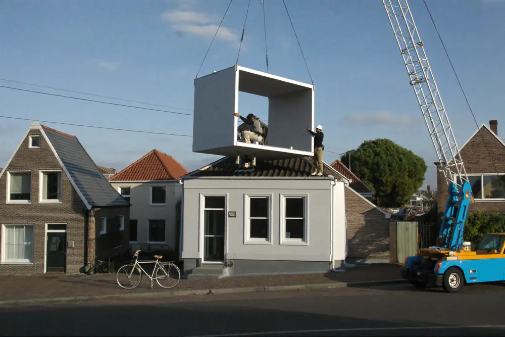Een prefab dakkapel hangt aan een mobiele kraan boven het dak van een rijtjeshuis